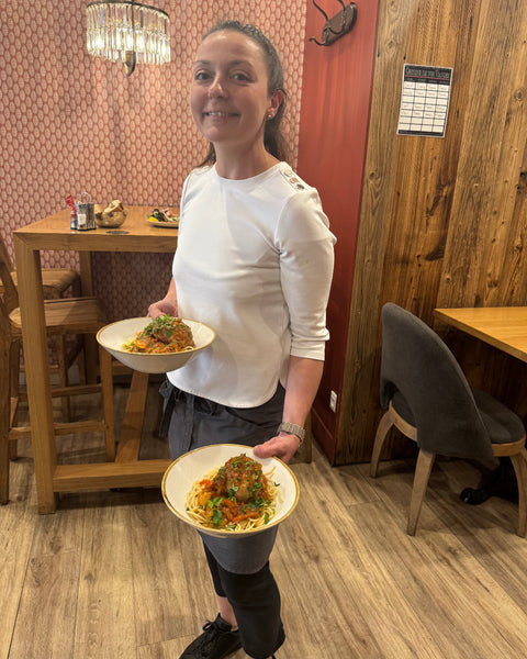 Serveuse souriante à la Brasserie Le Cathédrale Gourmand à Chartres, apportant deux assiettes généreuses de plat du jour dans une salle au décor chaleureux.