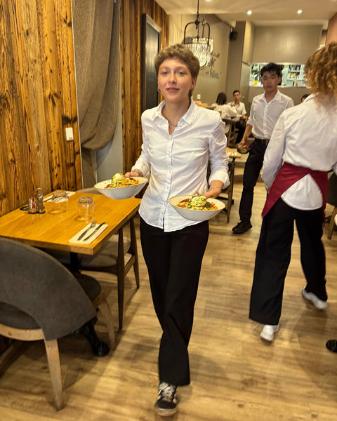 Serveuse souriante en plein service à la Brasserie Le Cathédrale à Chartres, apportant deux assiettes garnies dans une salle chaleureuse au décor bois.

